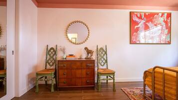 A room with a wooden dresser, two chairs, a mirror, and a large framed picture on the wall.