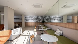 Een modern interieur met een zithoek, tafels en een groot abstract wandkunstwerk.