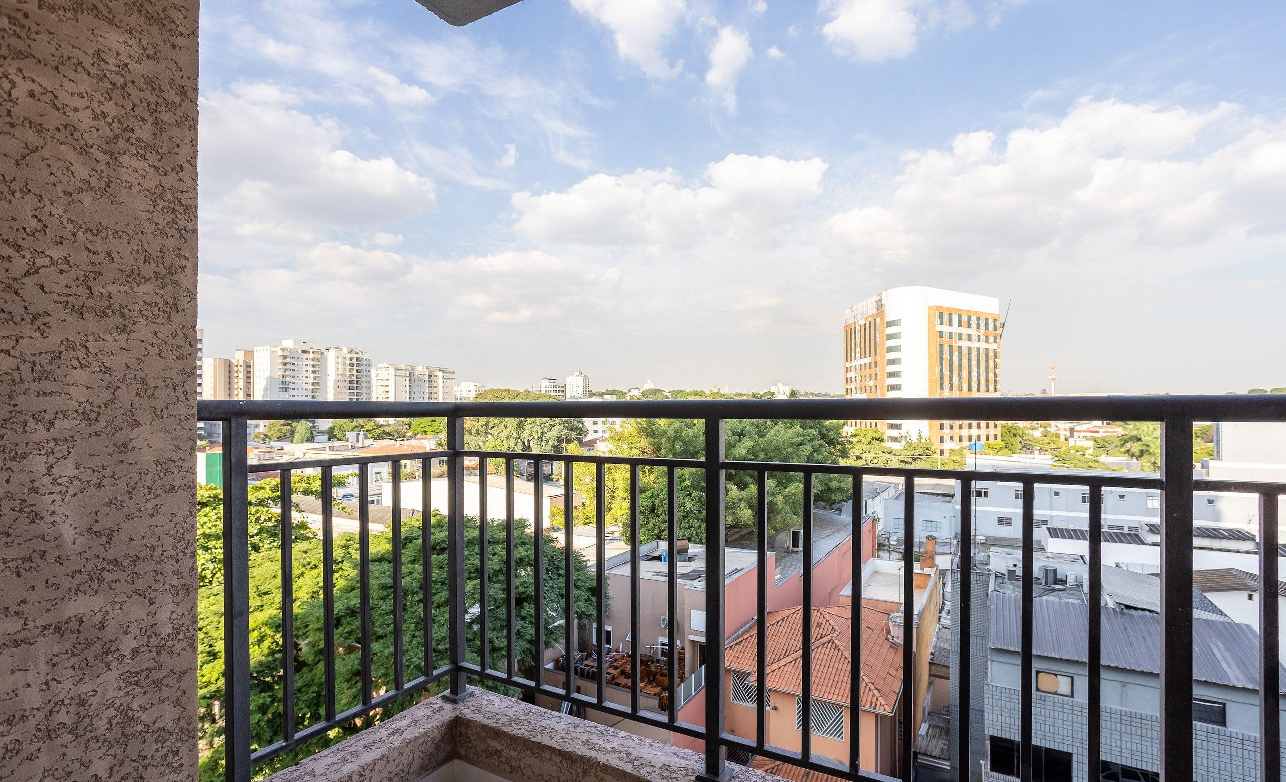 Uma varanda com vista para edifícios e vegetação ao redor.