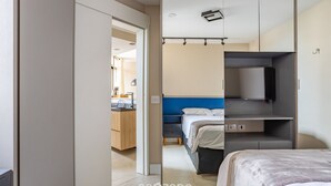 A modern bedroom with a bed, a TV, and a wardrobe. There is a kitchenette in the background. -  1 Bedroom Apartment with pool 600m from Moema/SP metro station NPZ093 (São Paulo)