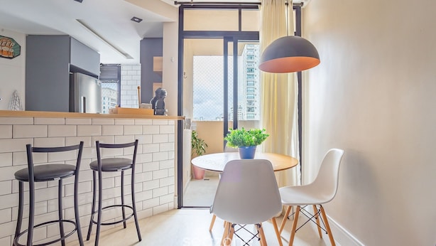 A modern kitchen with a built-in refrigerator, a dining area with a round table and chairs, and a view of a cityscape through a large sliding door. -  1 Bedroom Apartment with pool 600m from Moema/SP metro station NPZ093 (São Paulo)