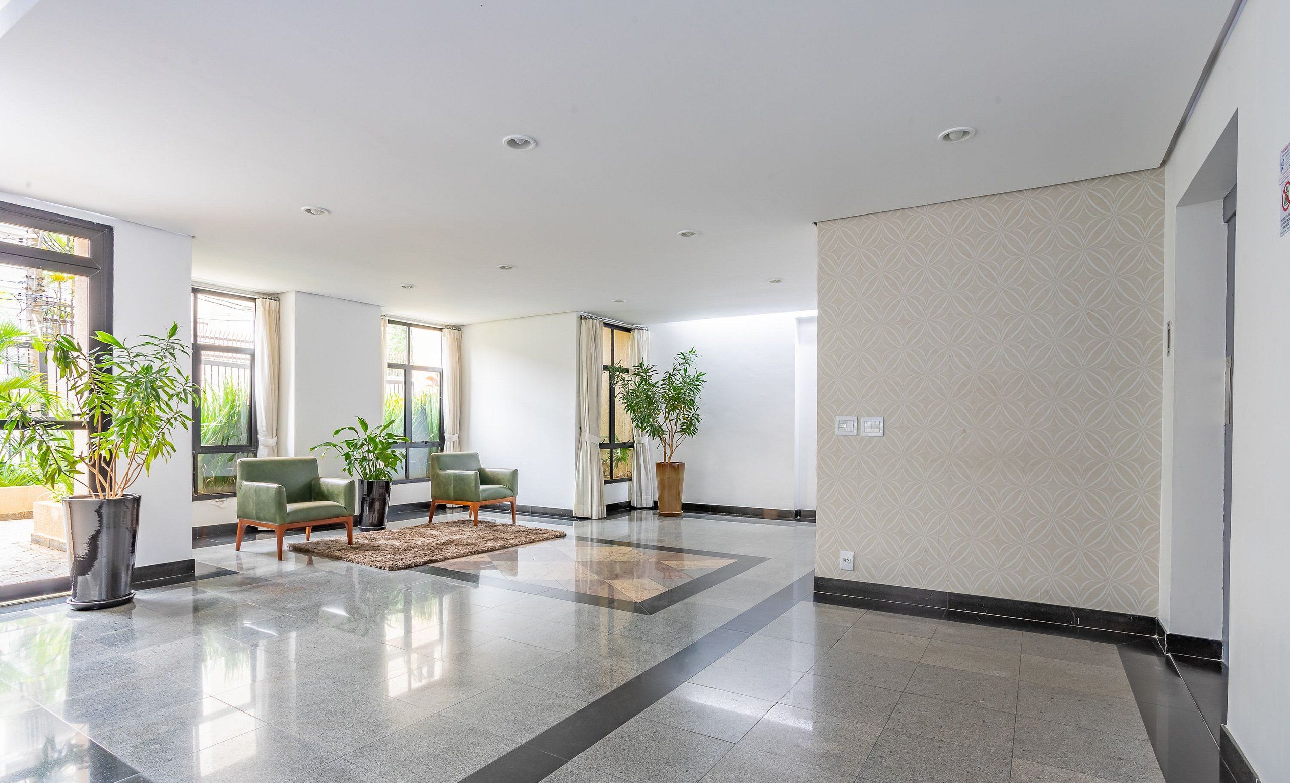A spacious lobby with a polished tile floor, green armchairs, and potted plants.