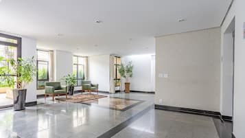 Um hall amplo com chão de azulejos brilhantes, poltronas verdes e plantas em vasos.