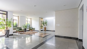 A spacious lobby with a polished tile floor, green armchairs, and potted plants. -  1 Bedroom Apartment with pool 600m from Moema/SP metro station NPZ093 (São Paulo)