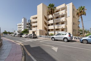 Un immeuble à plusieurs étages doté de balcons, avec des voitures garées et des palmiers.