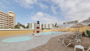 A rooftop pool area with lounge chairs, a pool, and a view of surrounding buildings.