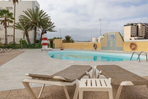 Un espace piscine avec des chaises longues, des palmiers et une bouée de sauvetage fixée au mur.