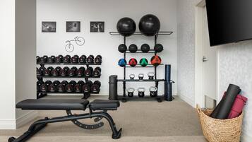 Un gimnasio en casa con una banca, mancuernas, kettlebells y un televisor montado en la pared.