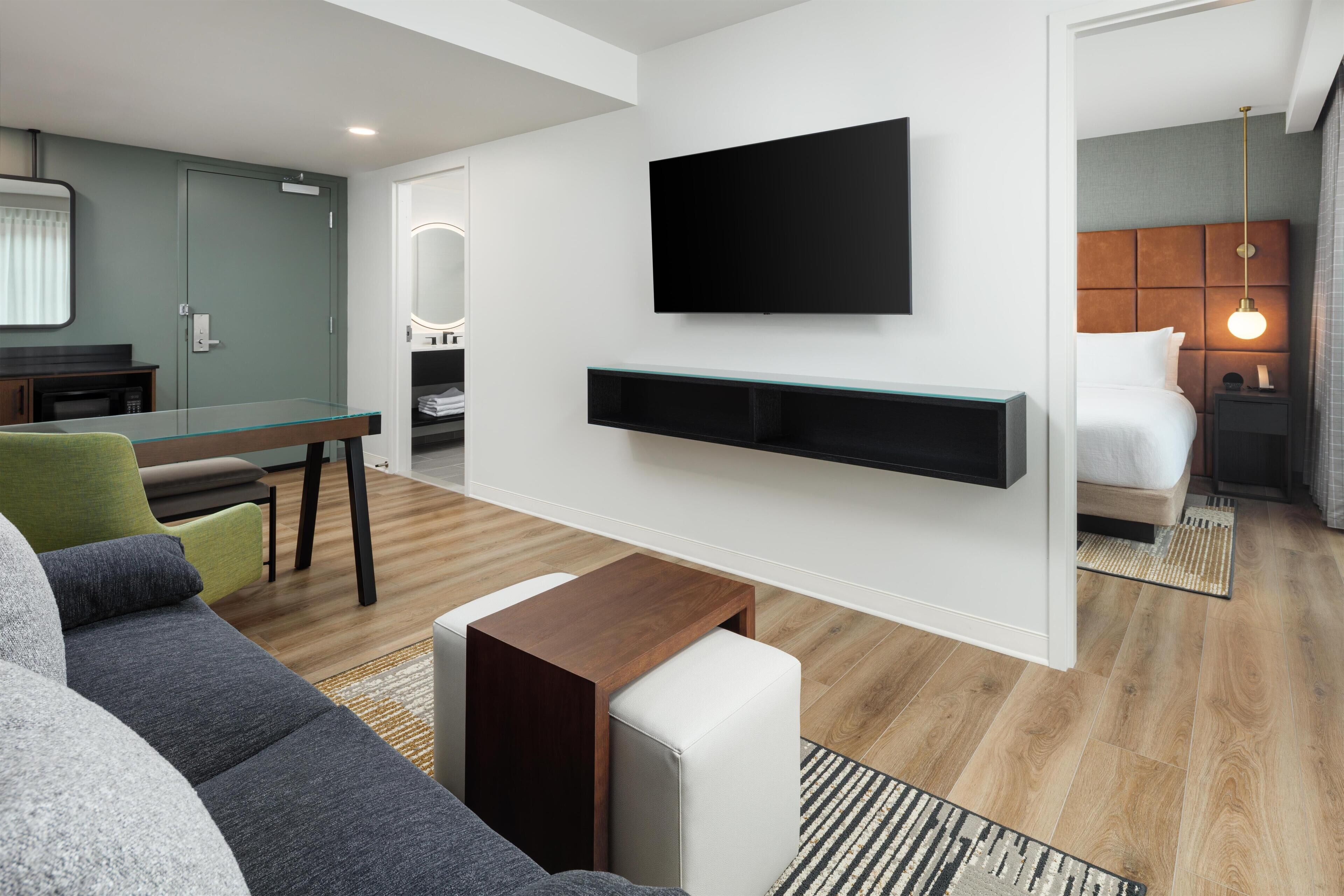 Una habitación de hotel moderna con televisión de pantalla plana, un sofá, una mesita y una cama con cabecero.