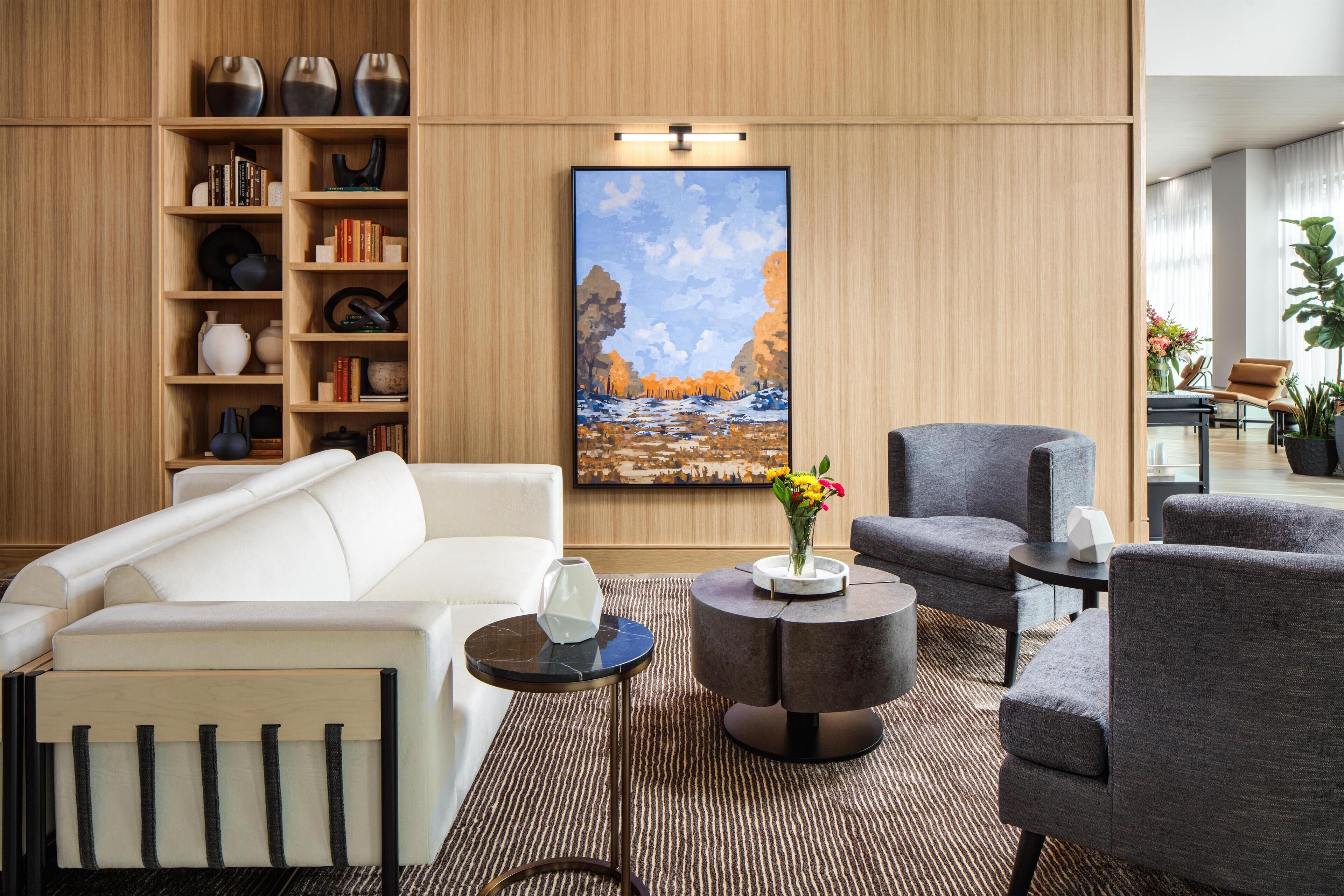A modern living room with a white sofa, grey armchairs, a coffee table, and a bookshelf filled with books and decorative items.