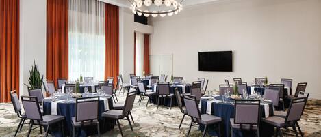 A conference room with round tables, chairs, and a large chandelier.
