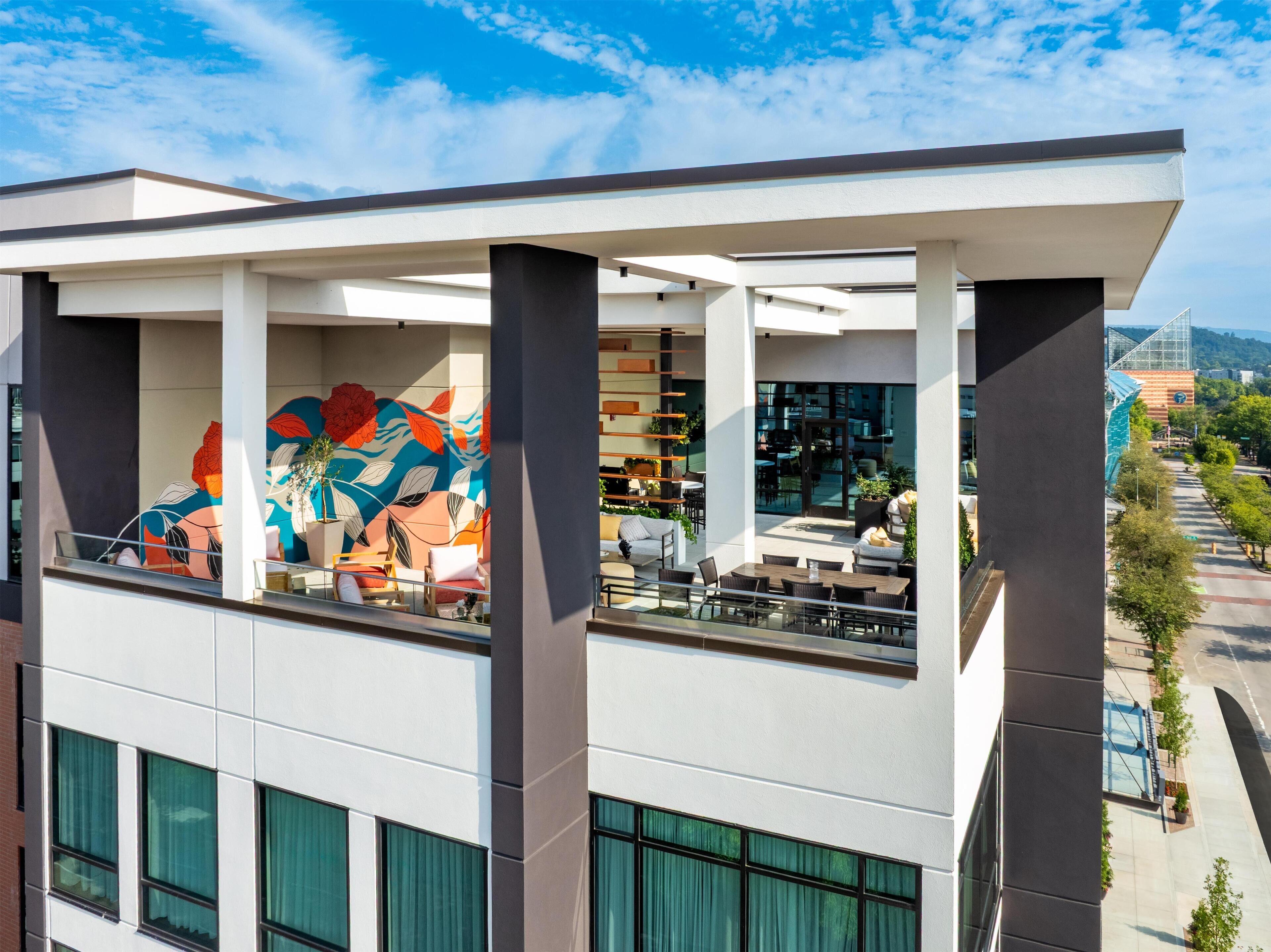 A modern building with a rooftop patio area featuring outdoor seating and a colorful mural.