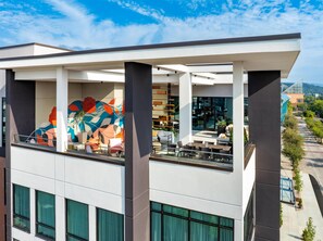 Un edificio moderno con un patio en la azotea, con mesas al aire libre y un mural colorido.