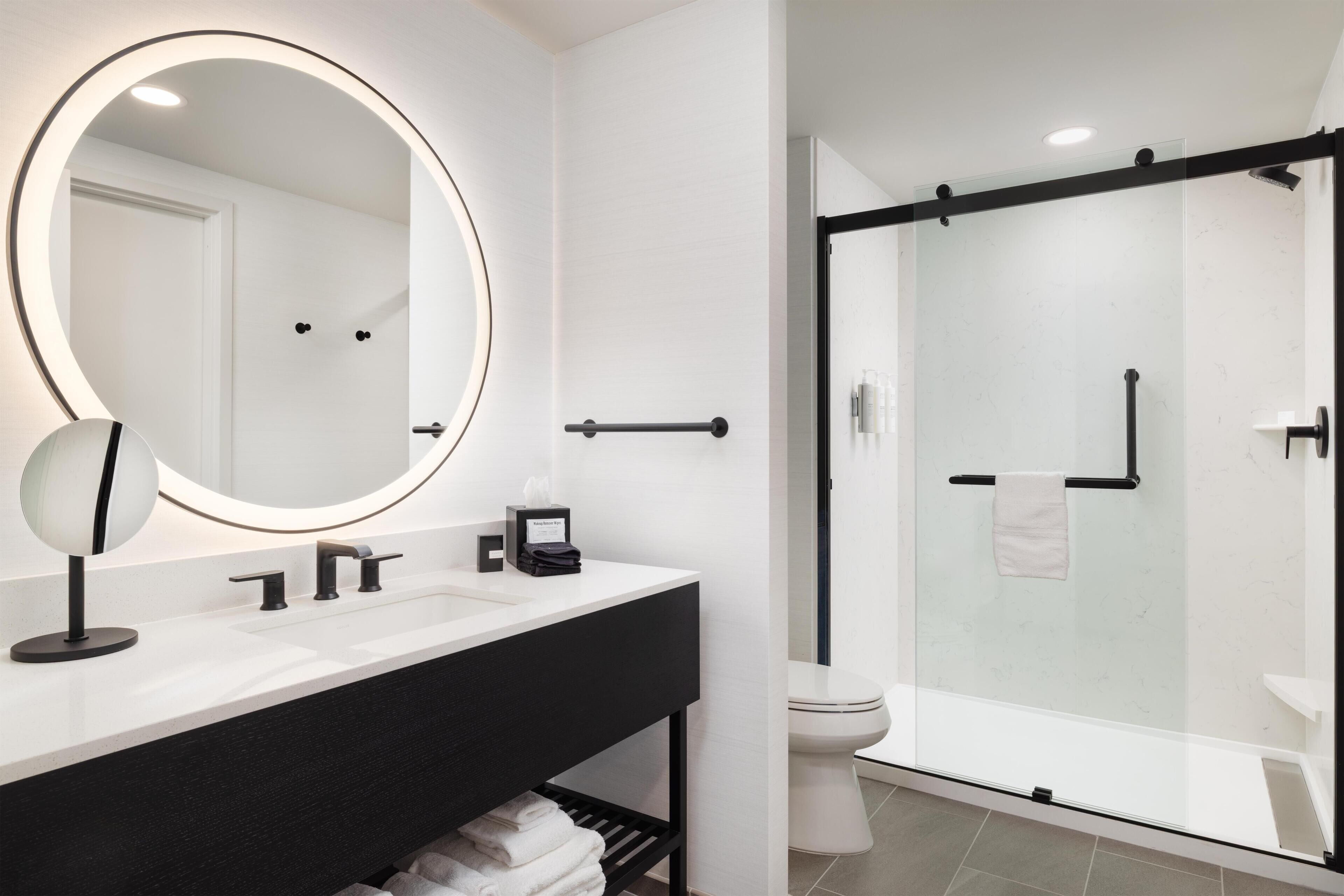 A modern bathroom with a large mirror, a black vanity, a glass shower enclosure, and a white toilet.