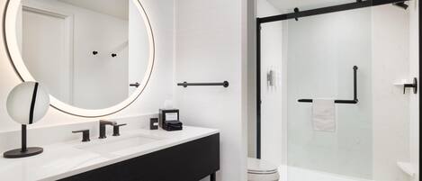 A modern bathroom with a large mirror, a black vanity, a glass shower enclosure, and a white toilet.