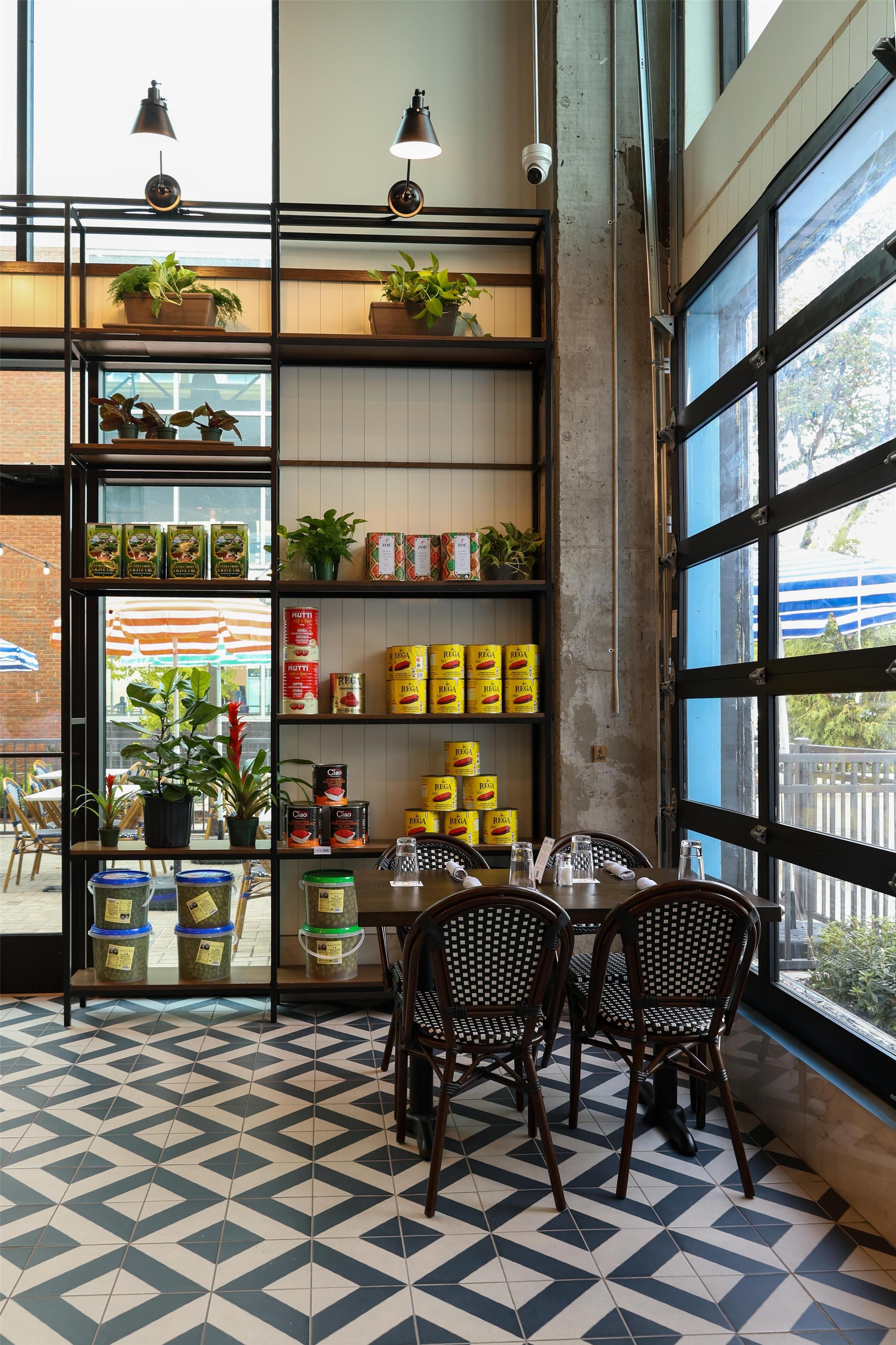 A cafe interior with a dining area, shelves stocked with canned goods, and potted plants.