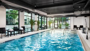 An indoor swimming pool with clear windows, lounge chairs, and potted plants. - Embassy Suites By Hilton Chattanooga Downtown (Chattanooga)