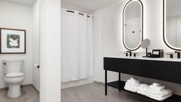 Une salle de bain moderne avec des toilettes, un rideau de douche, un meuble-lavabo avec un miroir et des serviettes soigneusement pliées sur une étagère.