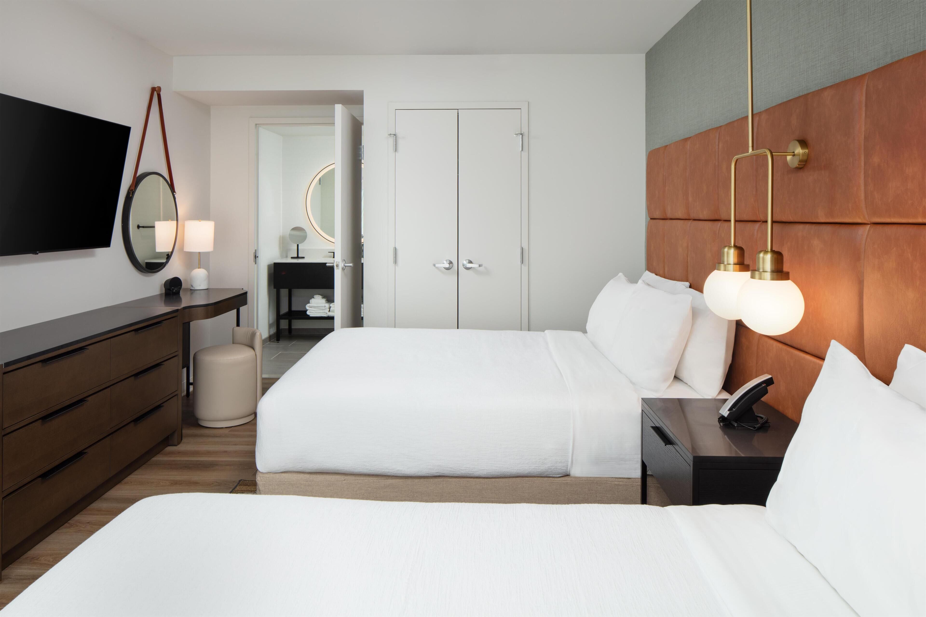A hotel room with a large bed, a bedside table with a lamp, a TV mounted on the wall, and a wardrobe.