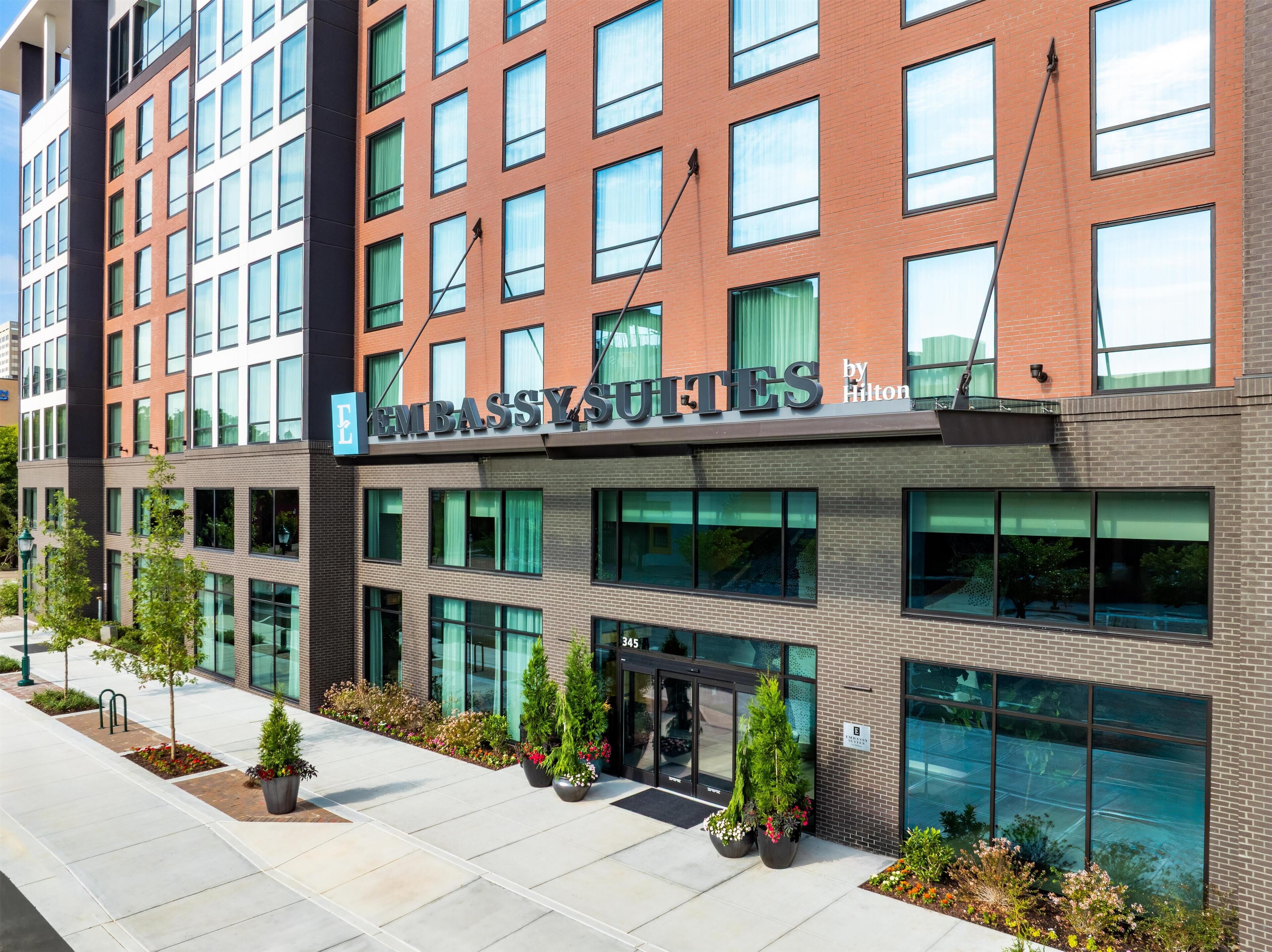 A modern hotel with a brick facade, large windows, and a sign indicating it's a Hilton property.