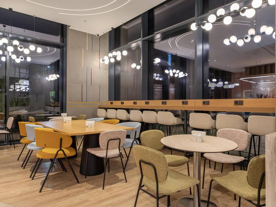 Un comedor moderno con mesas y sillas redondas, iluminación colgante y ventanas amplias.