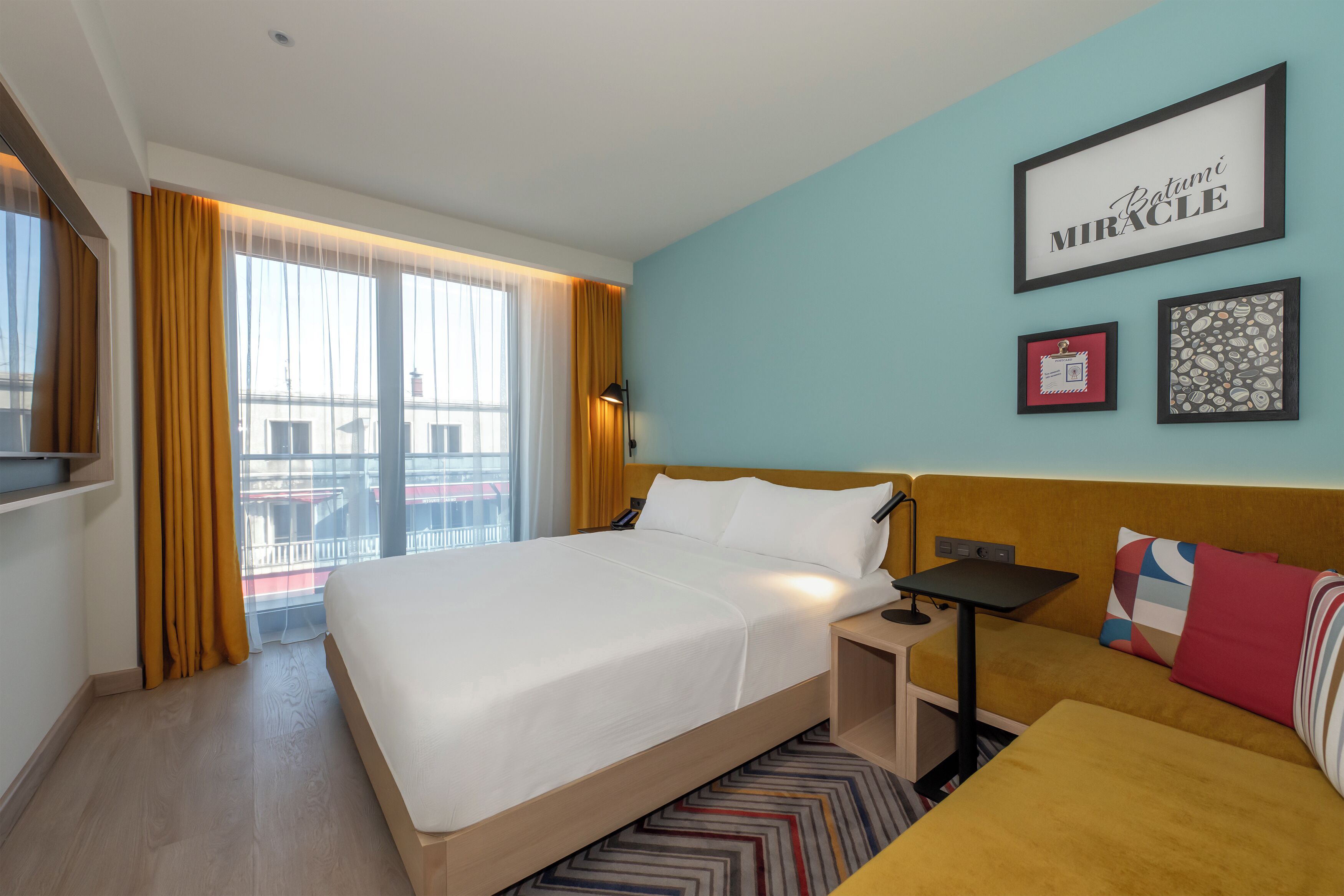 A hotel room with a large bed, a sofa, a desk, and a window with curtains.
