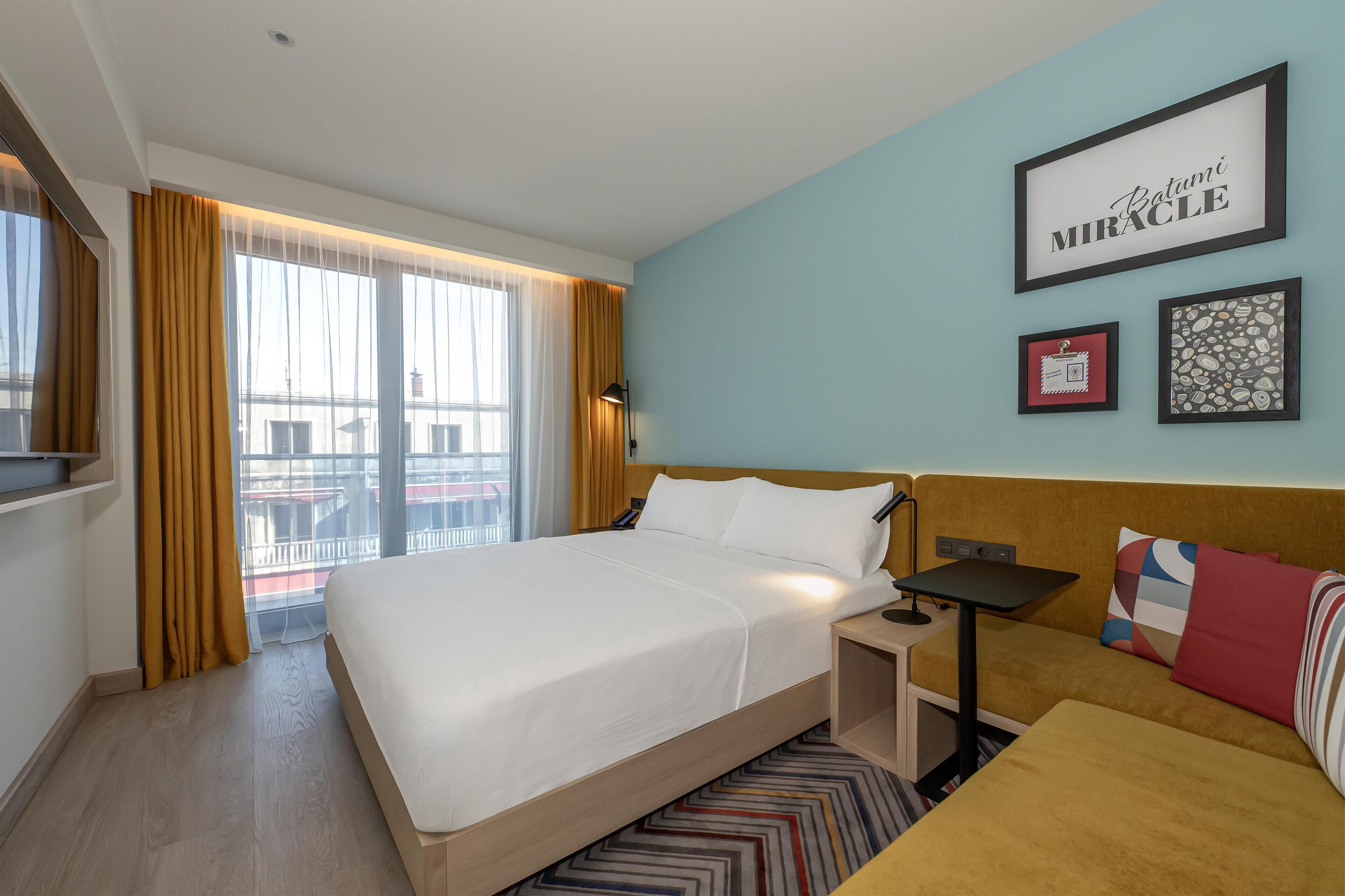 Hotellihuone, jossa on suuri sänky, sohva, pieni pöytä ja seinä, jossa on kehystettyjä kuvia.