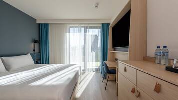 Habitación de hotel con cama, escritorio, silla, televisor y vista a la ciudad desde la ventana.