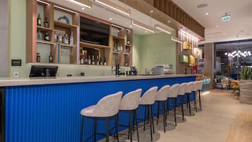 A bar area with a blue counter, bar stools, and shelves with bottles and glasses.