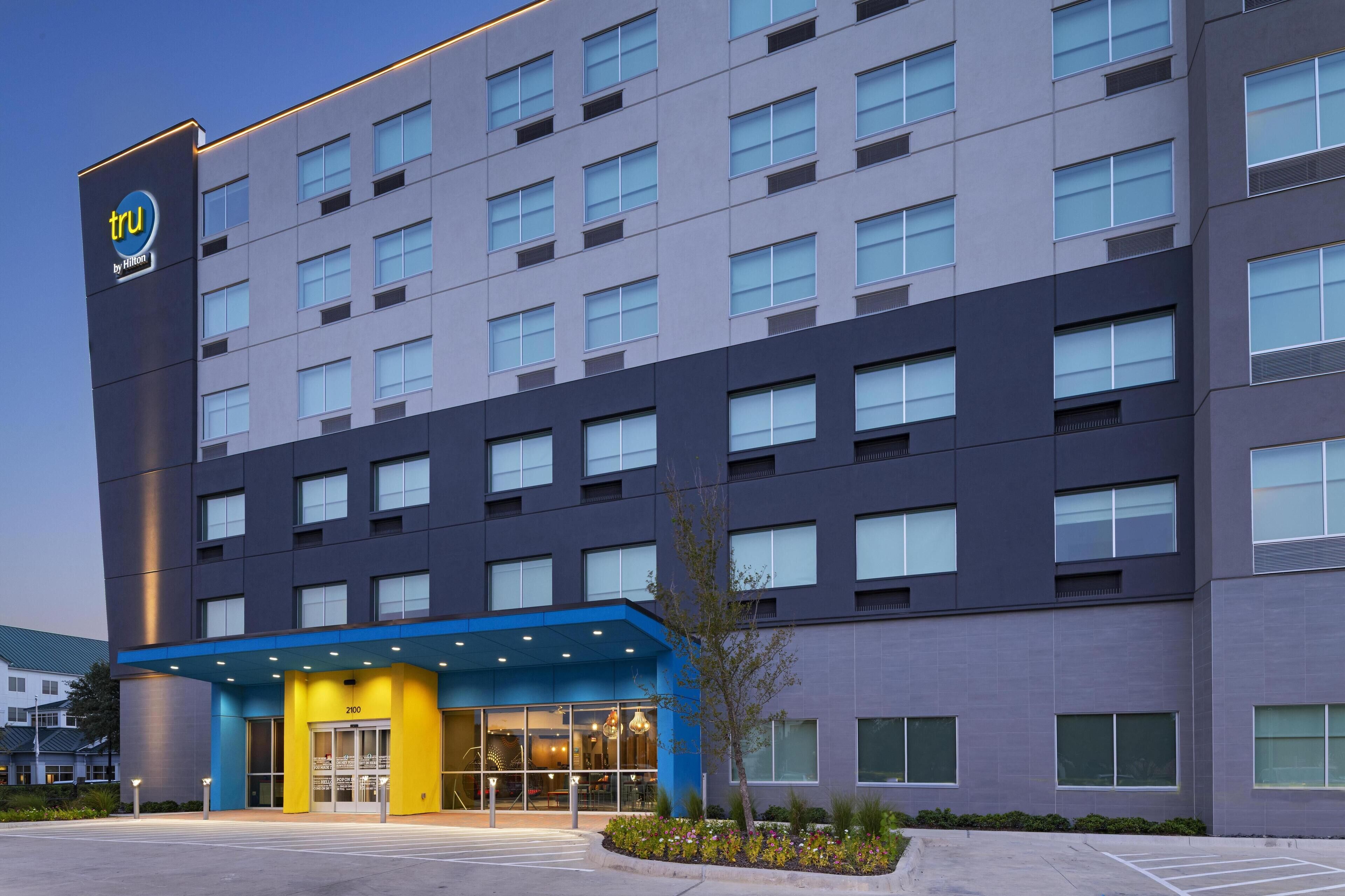 Un hotel moderno con un toldo azul en la entrada, varios pisos y un llamativo logotipo 'tru'.
