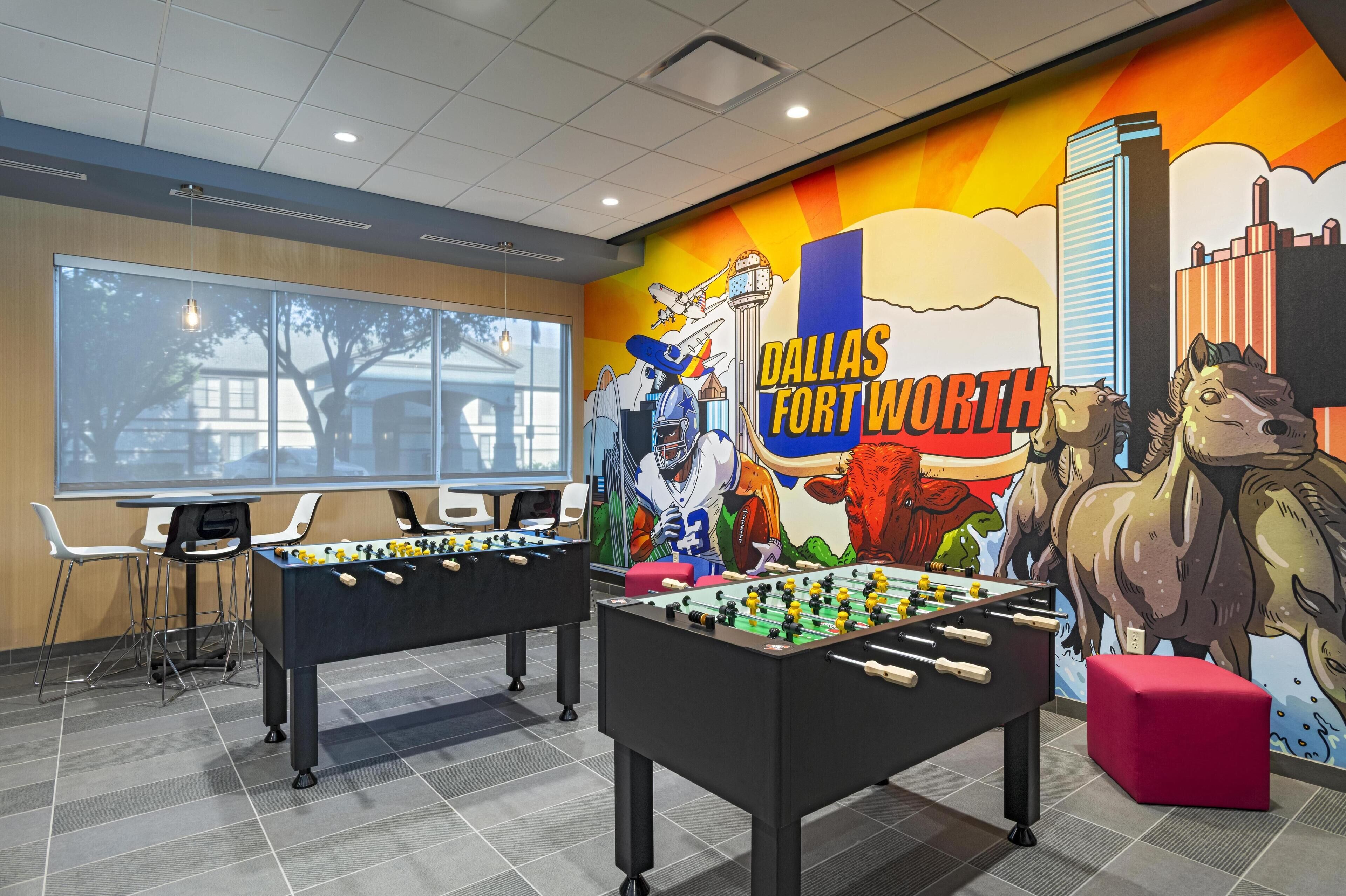 Una habitación con dos mesas de fútbol de mesa, un mural de Dallas Fort Worth y un ventanal grande.