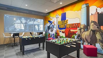 Una habitación con dos mesas de fútbol de mesa, un mural de Dallas Fort Worth y un ventanal grande.