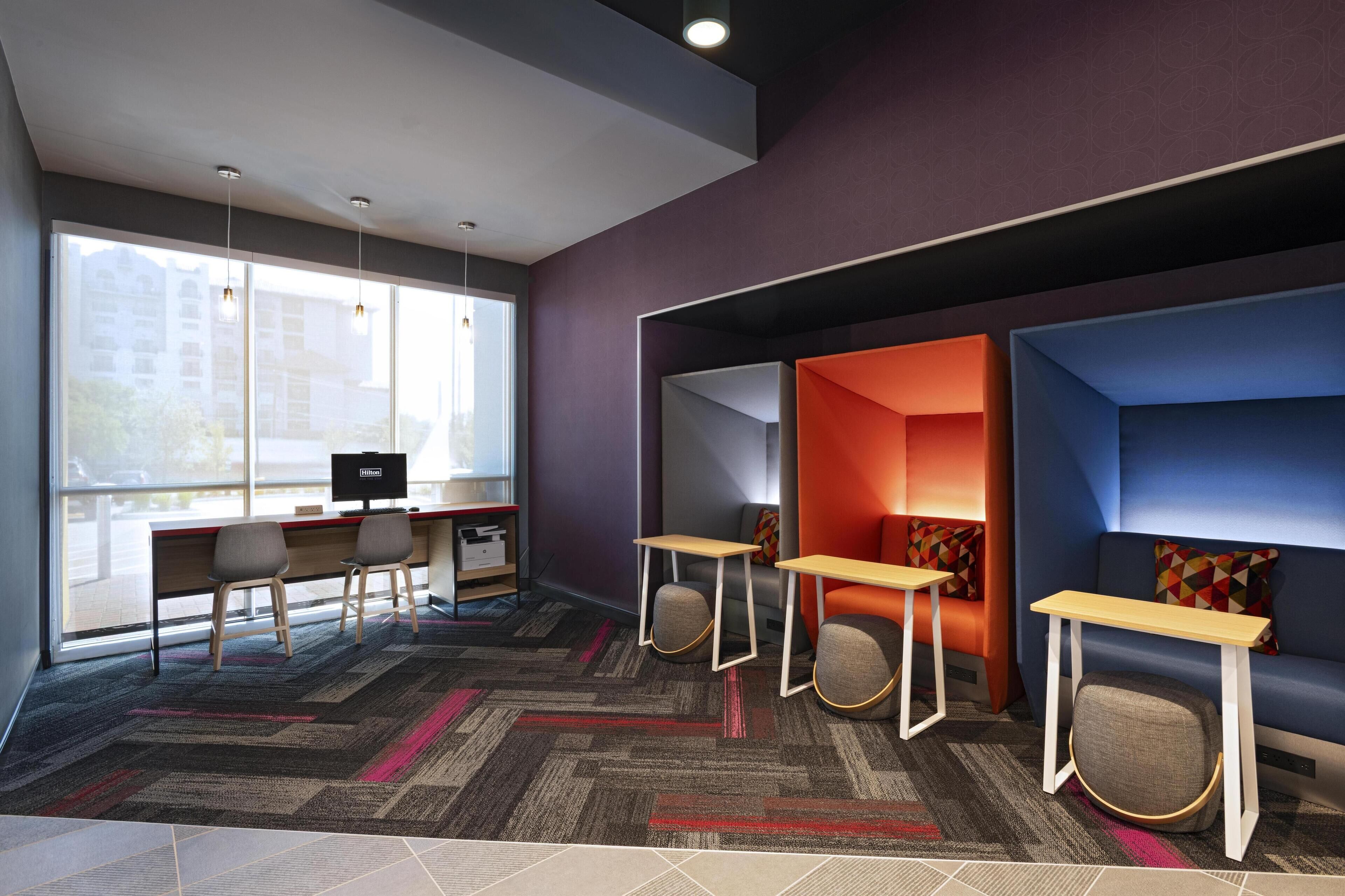 A modern office space with a large window, two desks with chairs, and a blue sofa with a small table.