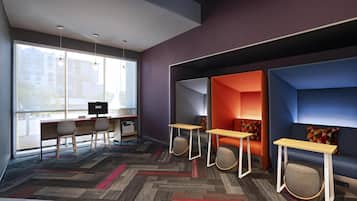 A modern office space with a large window, two desks with chairs, and a blue sofa with a small table.