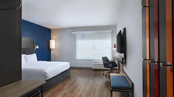 Ein Hotelzimmer mit Bett, Schreibtisch, Stuhl, Fernseher und einem Fenster mit Jalousien.