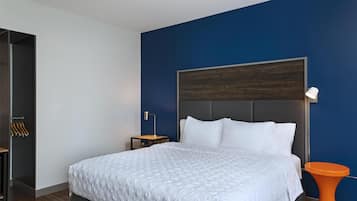 Un dormitorio moderno con una cama grande, una mesita de noche, una lámpara y una mesita auxiliar naranja brillante.