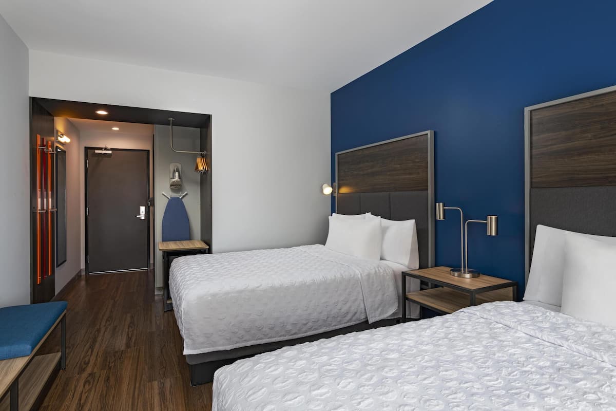 A hotel room with two beds, a desk, a chair, and a bathroom visible through an open door.