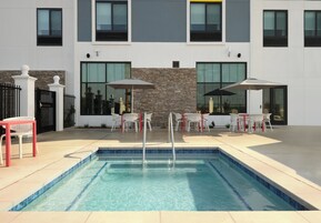 Una piscina con una pared de piedra y mobiliario moderno para exteriores, incluyendo sillas y sombrillas.