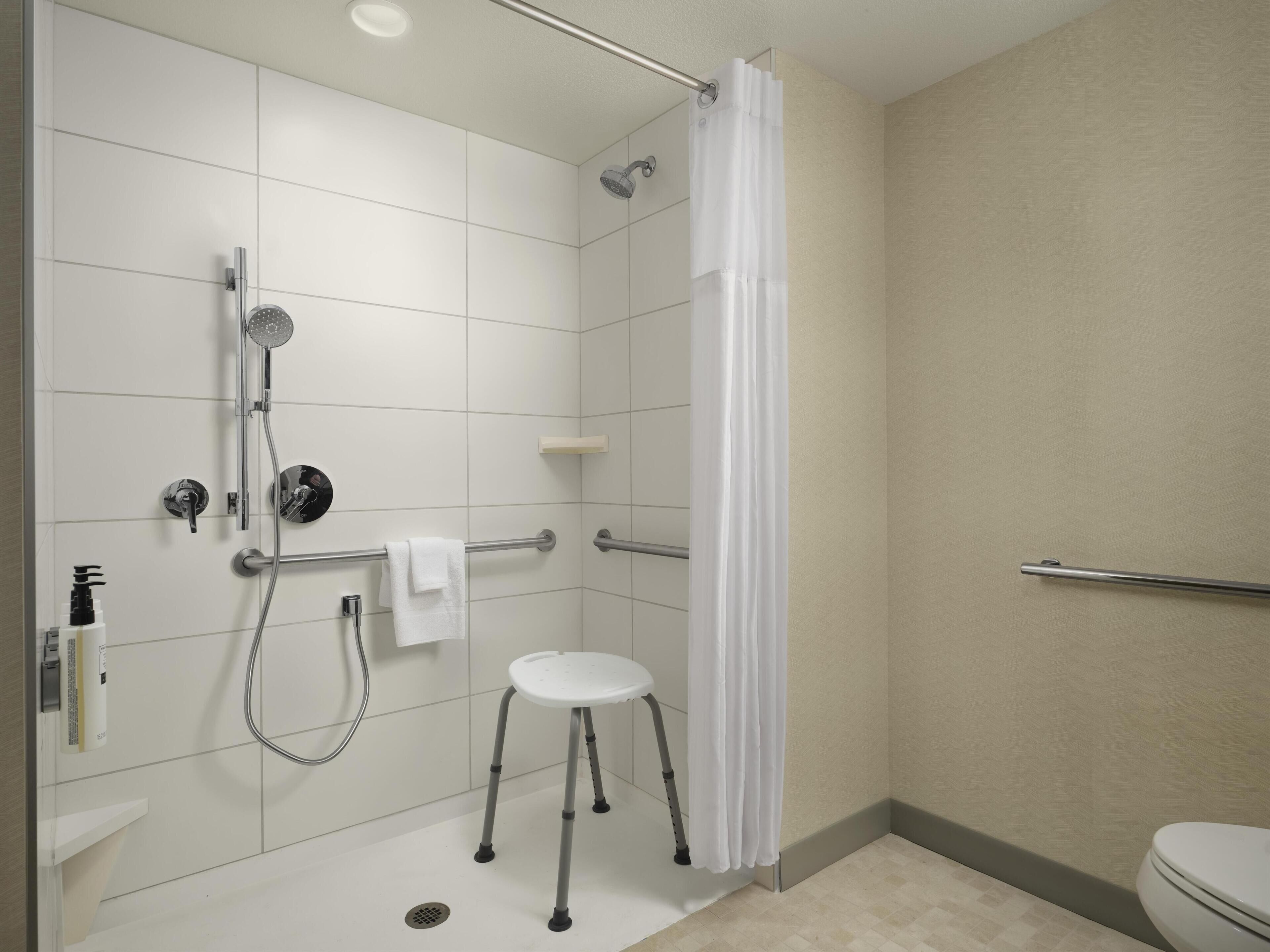 Une salle de bain moderne équipée d’une douche, de toilettes et d’un petit tabouret blanc.
