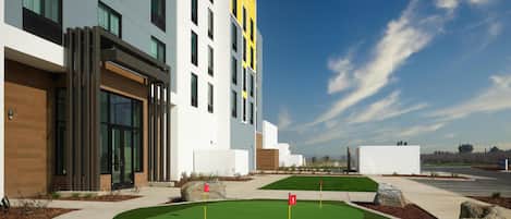 A modern building with a flat roof, large windows, and a well-maintained lawn with a putting green.