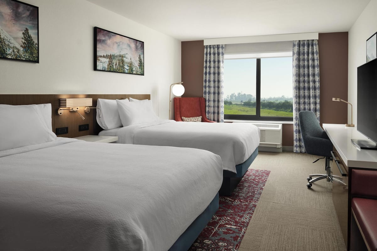 Une chambre d’hôtel avec deux lits, un bureau, une chaise, une télévision et une grande fenêtre donnant sur un beau paysage.