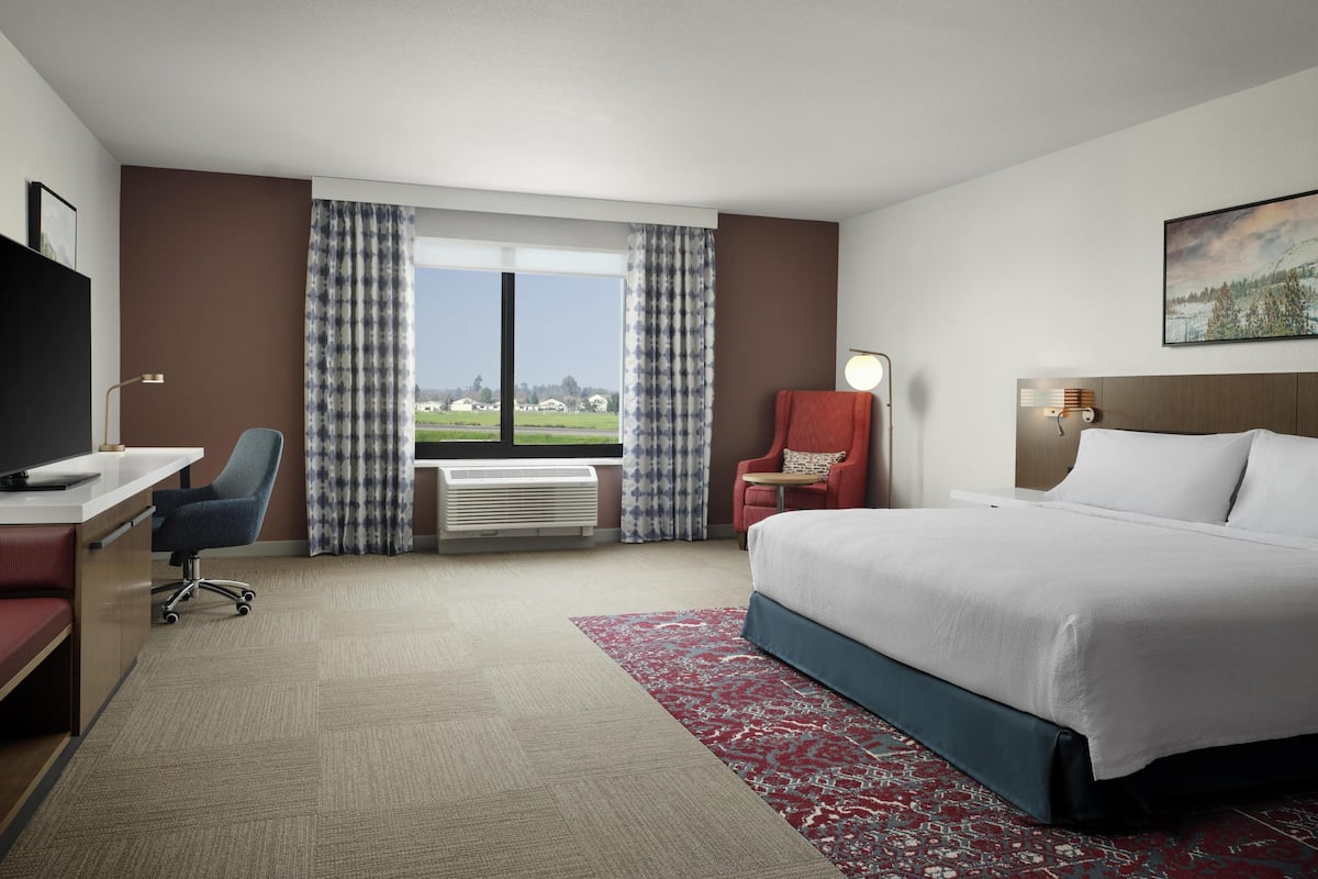 Une chambre d’hôtel avec un lit, un bureau, une chaise et une grande fenêtre avec des rideaux.