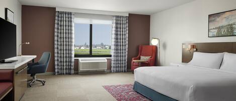 A hotel room with a bed, desk, chair, and a large window with curtains.
