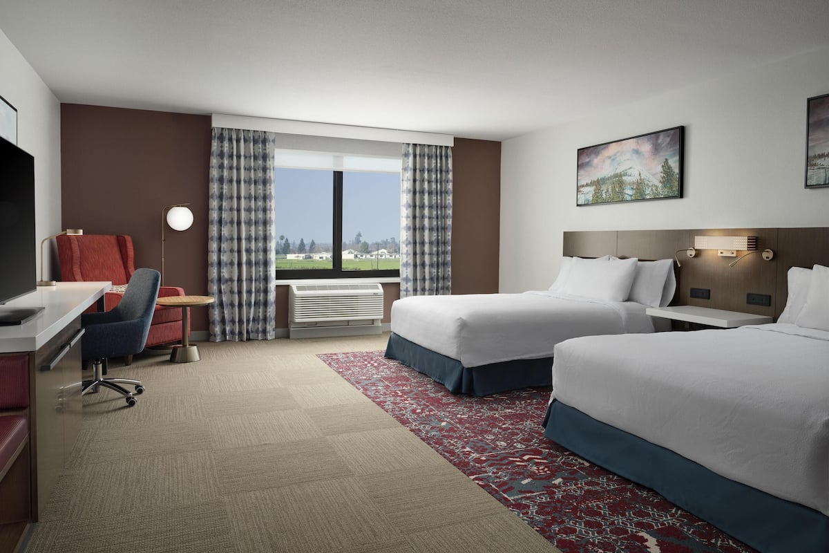 Une chambre d’hôtel avec deux lits, un bureau, une chaise, une télévision et une fenêtre avec des rideaux.