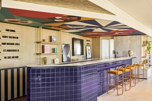 A bar area with a blue-tiled counter, wooden shelves, and a colorful ceiling mural. - Hampton by Hilton Lyon Airport (Colombier-Saugnieu)