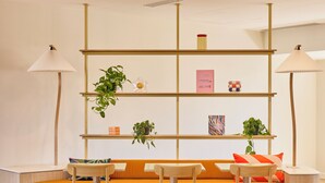 Een moderne, goed verlichte kamer met een houten bank, bijpassende stoelen en een boekenkast met planten en boeken.