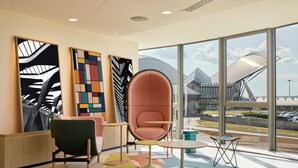 Een modern interieur met een groot raam, een groene stoel, een roze stoel en een kleurrijk vloerkleed.