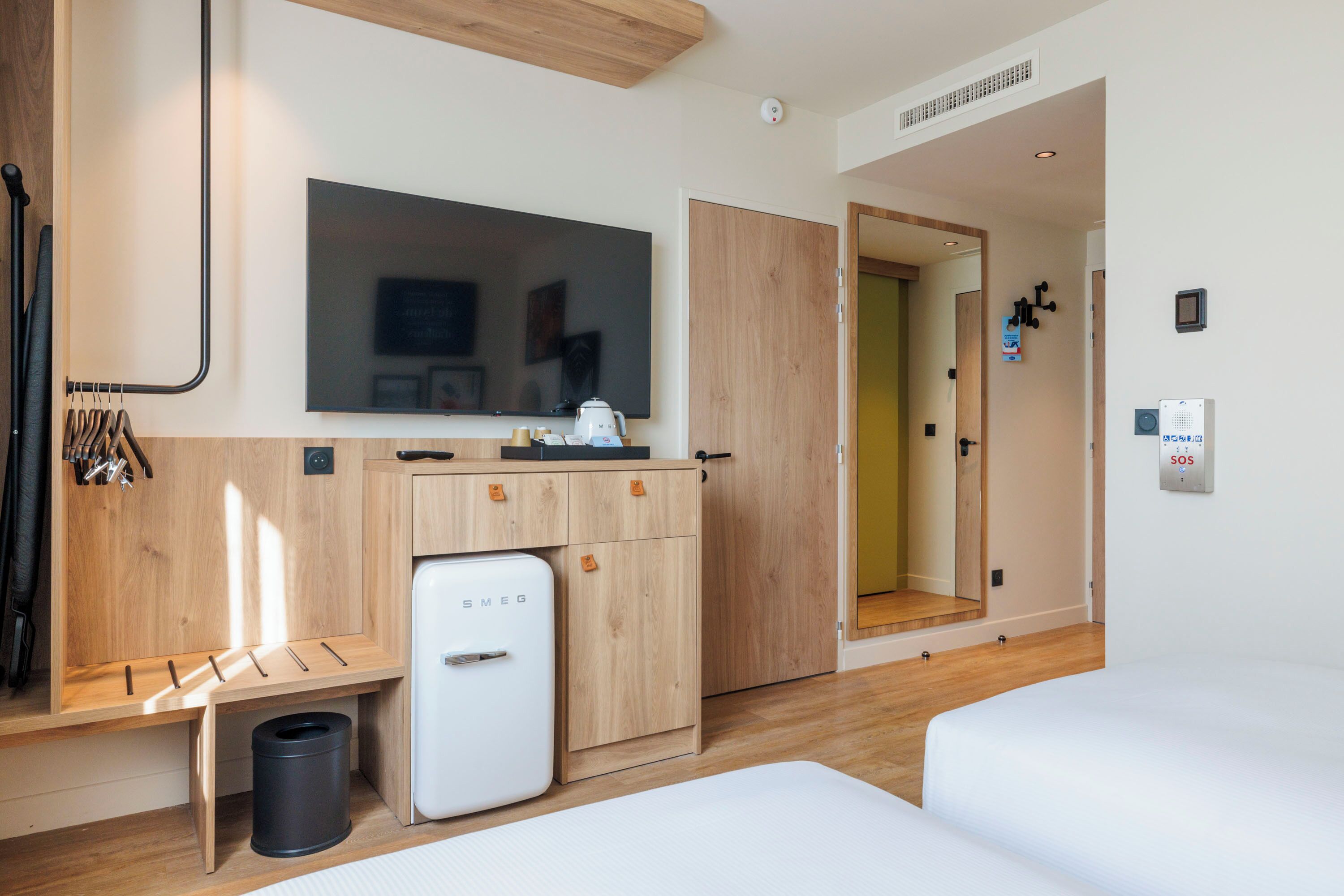 Een hotelkamer met een bed, een kleine koelkast, een aan de muur bevestigde televisie en een houten kast.