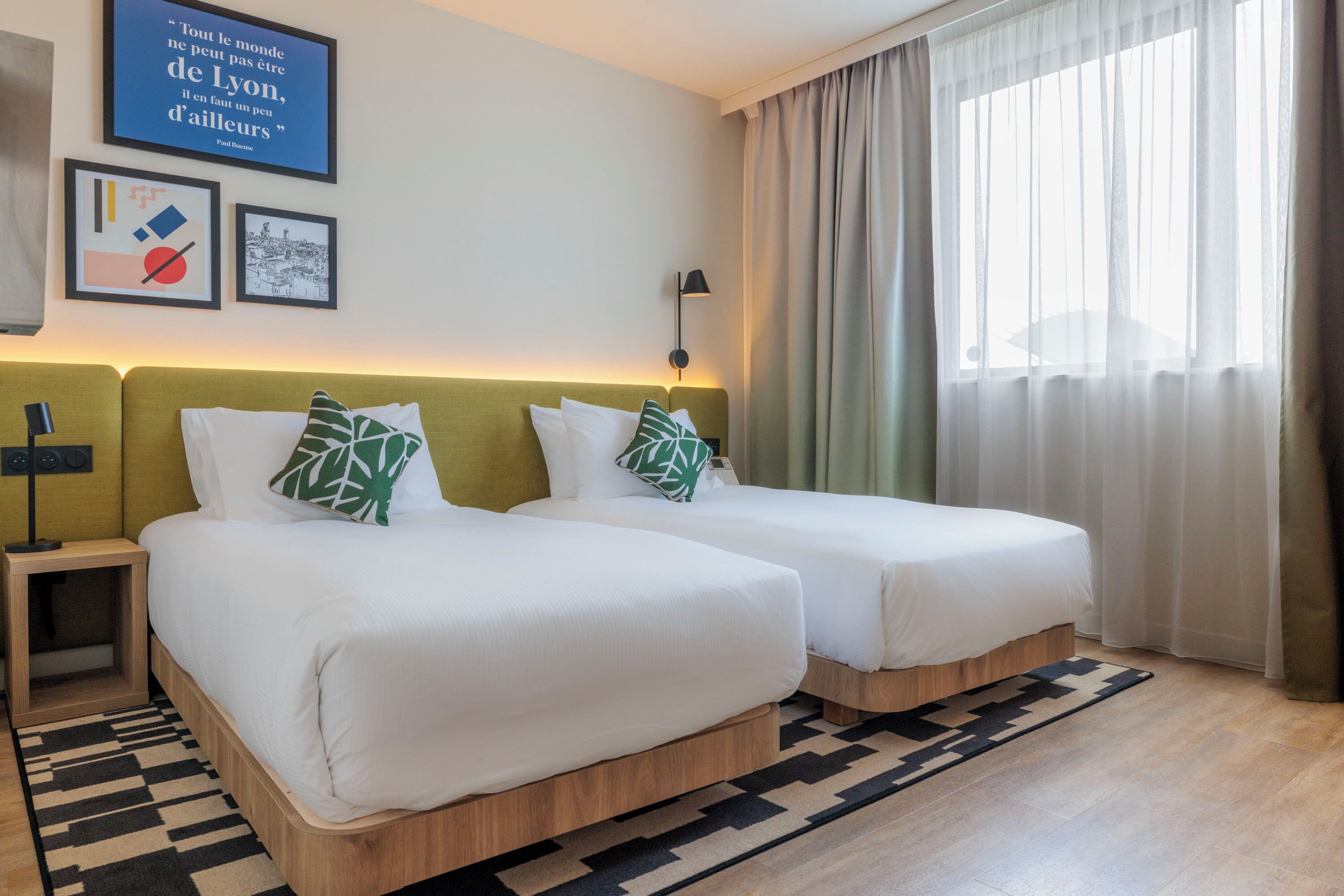 Een hotelkamer met twee bedden, een nachtkastje, een lamp en een groot raam met gordijnen.