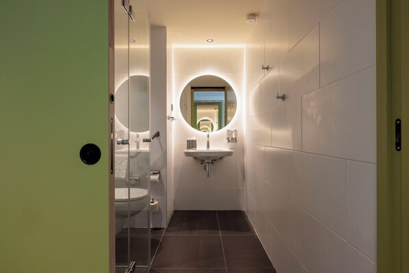 Un baño moderno con mampara de vidrio, un espejo redondo, un lavabo y un inodoro.